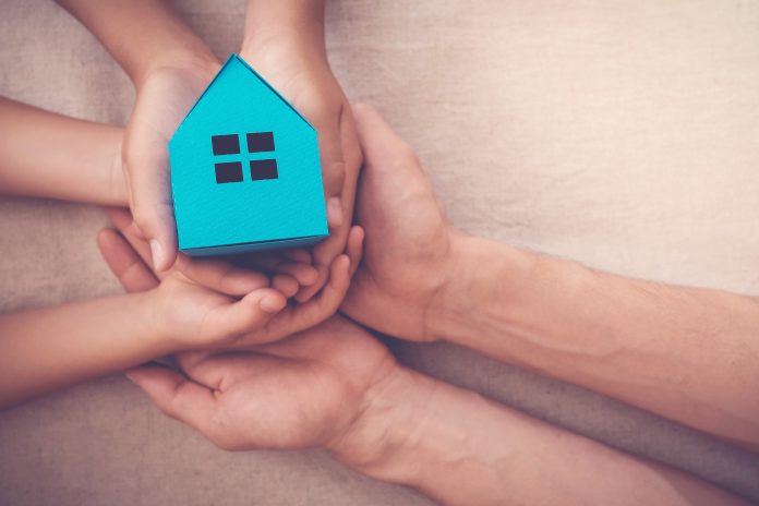 Adult and child hands holding blue paper house for family home and homeless shelter concept
